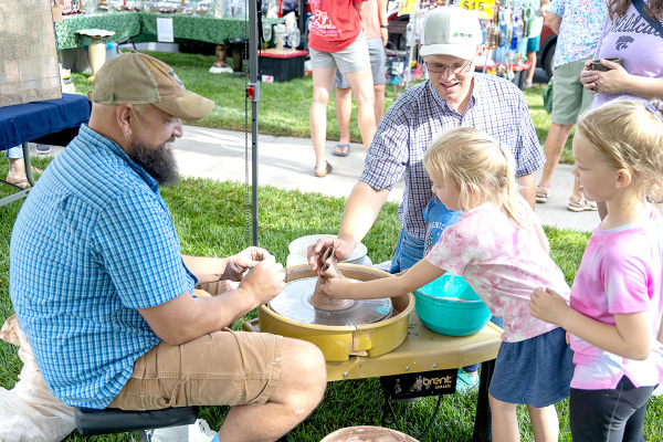 HANDS-ON FUN at the Fair! Artisan potter Rodney Zimmerman of Colby gives Garrett Kennedy and his daughters a spin at the pottery wheel during Saturday’s Hansen Museum Arts &amp; Crafts Fair. (Photo Credit: Clay Grammon, Prairie Sky Photography)