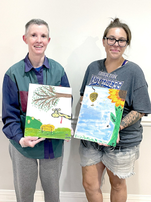 KAY BRUGGEMAN (left) and Jessica Owston display their completed masterpieces following the Stockton Public Library's Painting Roulette held July 24. During the creative event, each participant began with a painting on their own canvas before passing it around the room, where everyone added their own artistic touch. Kay's canvas started with a giraffe, while Jessica's began with a sunflower, with each evolving into a one-of-a-kind collaborative work of art by the end of the evening.