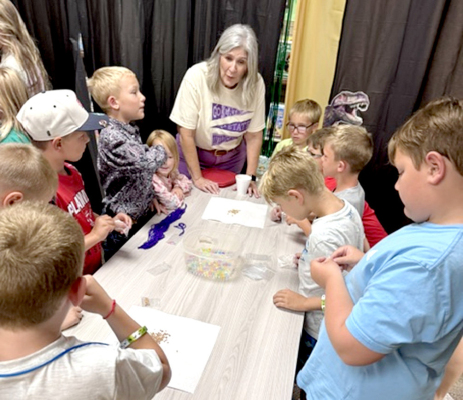 TAMMY MCCLELLAN from McClellan Farms teaching SLP kids how to make a seed necklace during Monday's UnEarth the Story of Kansas Wheat.