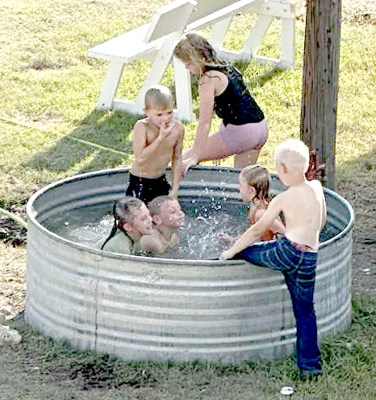 COOLING OFF, COUNTRY STYLE — kids splash and play in a stock tank at the Rooks County Free Fair, a scene captured by a reader hoping to stir fond memories of fairs gone by. Do any of you remember these days?