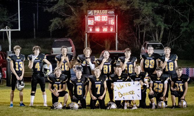 THE ROOSTERS ARE BACK! — The Palco Roosters celebrate Friday night’s historic 72-6 victory over Chase, their first win as an independent football program in nearly 15 years. With the final score shining on the scoreboard behind them, the Roosters proudly hold a sign declaring, “We’re Baaack!”