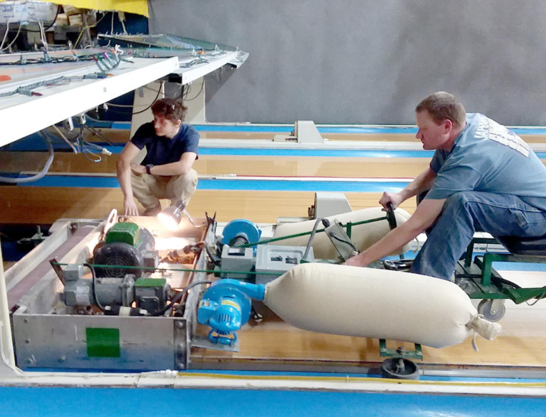 BRYAN SELTERS (on the machine) and Jared Strong (kneeling) work under the pinsetter, stripping down the area to the bare wood to make the lanes level and ready for the polyurethane coating.
