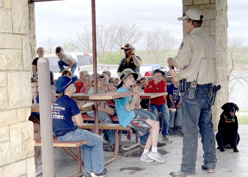 JAKE BROOKE, standing, explains to the large group of kids gathered what his K-9 friend, Kreed, does as a game warden’s dog.