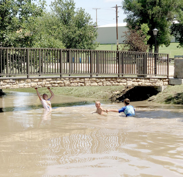 ISAAC THAYER, VINCE THAYER AND BENJAMIN WASSON enjoyed playing in Dibble Creek which runs through the Lower City Park early Monday afternoon following the heavy rain received the day before.