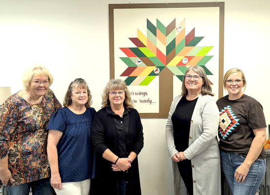 CELEBRATING CHERISHED MEMORIES, the vibrant memory quilt block wall hanging at Solomon Valley Manor honors the legacy of Jim Karns. Pictured from left to right are Jayne Prockish from The Sunflower Shed, Jim's daughters Martha Blair and Marianne Dix, alongside dedicated Solomon Valley Manor staff members Sheryl Kollman and Staci McClain. ( Plainville Times Photo)