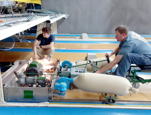 BRYAN SELTERS (on the machine) and Jared Strong (kneeling) work under the pinsetter, stripping down the area to the bare wood to make the lanes level and ready for the polyurethane coating.