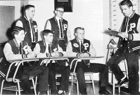 THE 1962 P-CLUB OFFICERS look over the plans for the year for the organization, which included a bus trip to Lawrence in November 1961 to watch the KU football squad take on the K-State team. Pictured are (seated, from left) stuco representative Mike Page, sergeant-at-arms Harold Huntzinger, vice president Ron Werner; (back row, standing) treasurer Roger Barta, and secretary Terry Kelly. President Mike Stahl is pictured on the right.