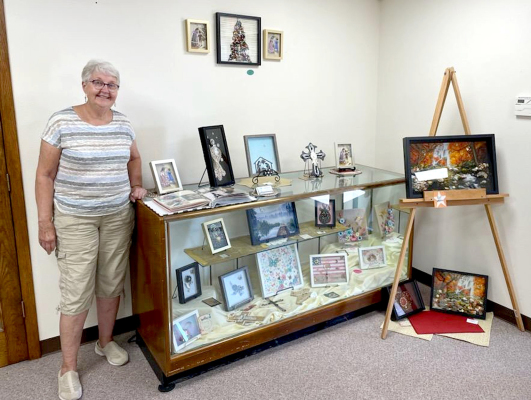 CINDY MCDOWELL stands next to her vintage jewelry shadow box creations. Her beautiful and creative art pieces will be on display at the museum for several weeks.