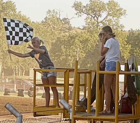 DURING THE HOT LAPS of the IMCA Stock Car Races at the Rooks County Free Fair on Wednesday night, flagman Micah Goscha took a little break and relinquished his duties to Delanee Bedore. Anyone familiar with Bedore knows she is a diehard race fan, so she was living the dream getting to wave the flags for the racers, one of whom was her father, Pat Bedore, Joining Delanee on the stand was her friend, Olivia Dix.