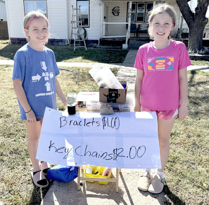 TAKING ADVANTAGE of a nice day, these two young ladies, Bridgette Axelson (left) and Norah Ganoung, were curbside selling bracelets and keychains on Sunday afternoon. (Photo Courtesy of Candace Rachel)