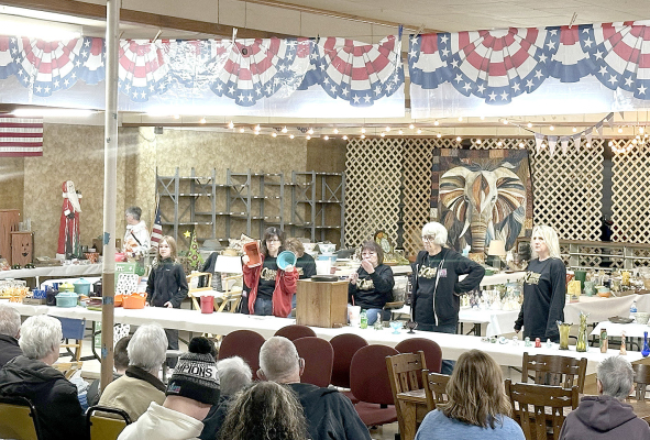 IT’S GENERATIONAL— Prairie Heritage Auction & Real Estate is one big family-whether related by blood or the bond of friendship. Pictured from the left in the background is an auction goer, standing behind the table Ivy Werner, daughter of Cole and Sara Werner and granddaughter of auction crew member Tammy Werner, Sheila (Selbe) Hachmeister, Lora (Selbe) Weigel , partically hidden behind Sheila, Susan (Selbe) Stahl, longtime crew member Paula Glick and Stephanie Nuss. (Courtesy Photo)