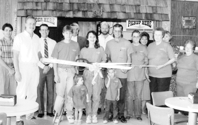 ON SEPTEMBER 27TH, 1991, the Grand Opening of KK Tacos and Burgers was held. Present at the ribbon cutting ceremony were (from left) Kent Hahn, Rusty Hrabe, Chris Kollman, Mark Kuhlmann, Myron Chapel, Mrs. Mark (Kathy) Kuhlmann, Nick Lowe, Dennis Kuhlmann, Mrs. Dennis (Sherry) Kuhlmann, Diane Strutt, Verna Mae Mauck, Linda Yohon, and Dot Hrabe. In front from left are Ashley Kuhlmann and Mitchell Kuhlmann.