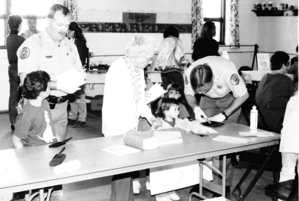 ROOKS COUNTY SHERIFF’S RESERVE OFFICER RANDY MOLL (right) helped fingerprint children for the Ident-A-Child table held at the 1991 Health Fair. He was assisted by Deputy Don Jenkins, Jr.