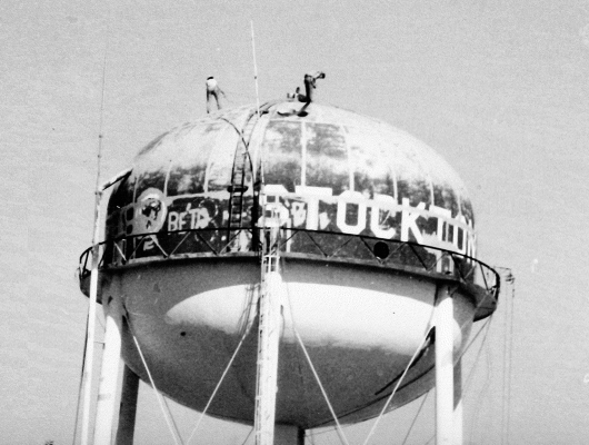 THE CITY’S WATER TOWER was painted in the Fall of 1989. This picture shows the two men priming the areas that had been sandblasted before the fresh coat of blue paint was applied.